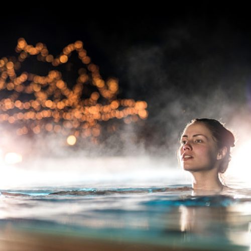 Young woman swimming in heated swimming pool during winter night.